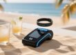 Professional overhead shot of NFC wristband tapping on a sleek, sand-colored payment terminal beside tropical drink glasses and palm leaf motif — no text or logos