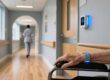 Professional healthcare setting with RFID wristband on elderly wrist, fixed RFID reader mounted at doorway, clean blue-gray interior lighting