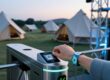Attendee scanning RFID fabric wristband at multi-day festival entry gate with camping and stage areas